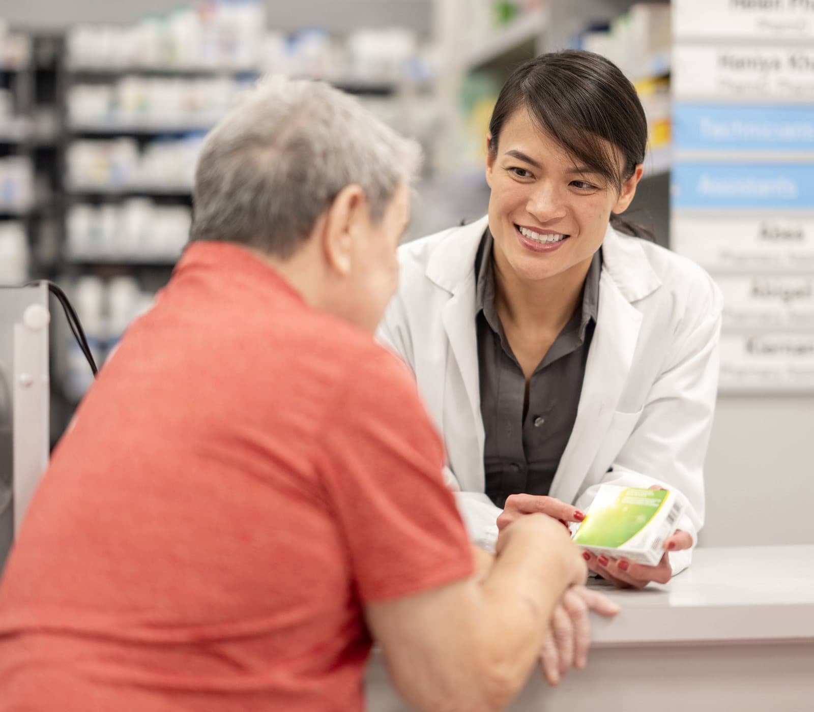 A pharmacist in a lab coat talking with a patient at the pharmacy counter
